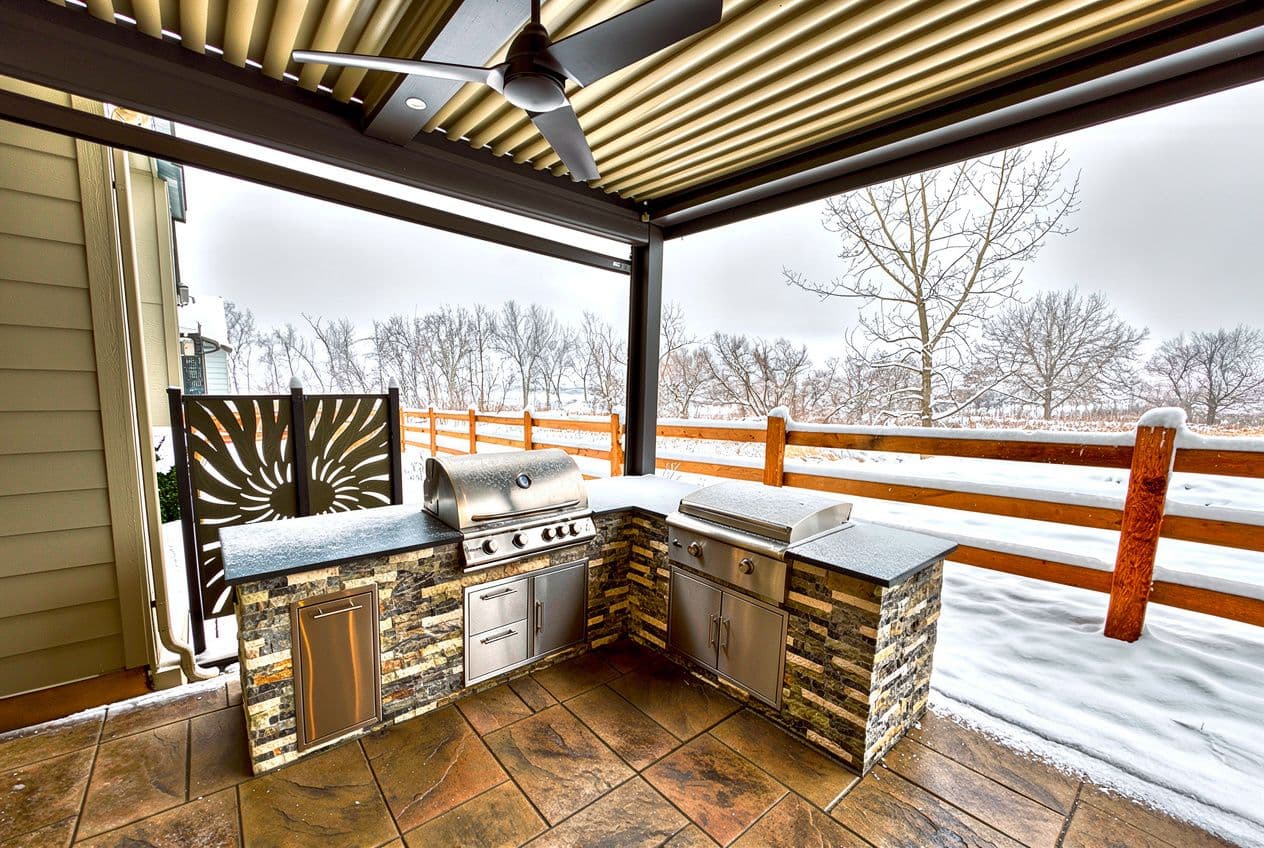 An outdoor kitchen on a covered patio in Colorado that looks out onto snow-covered trees and ground.